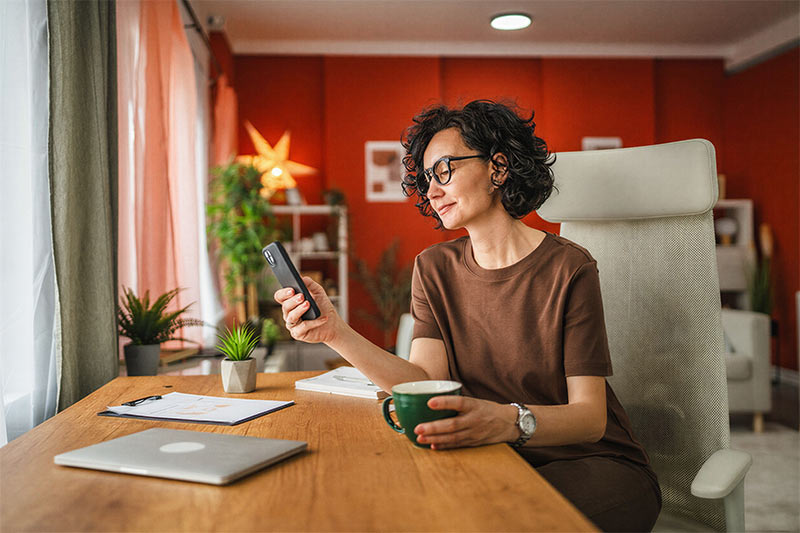 A female entrepreneur reviewing her financial plan on a smartphone in a modern office, representing Bircher Financial's commitment to modern efficiency and accessible expertise.